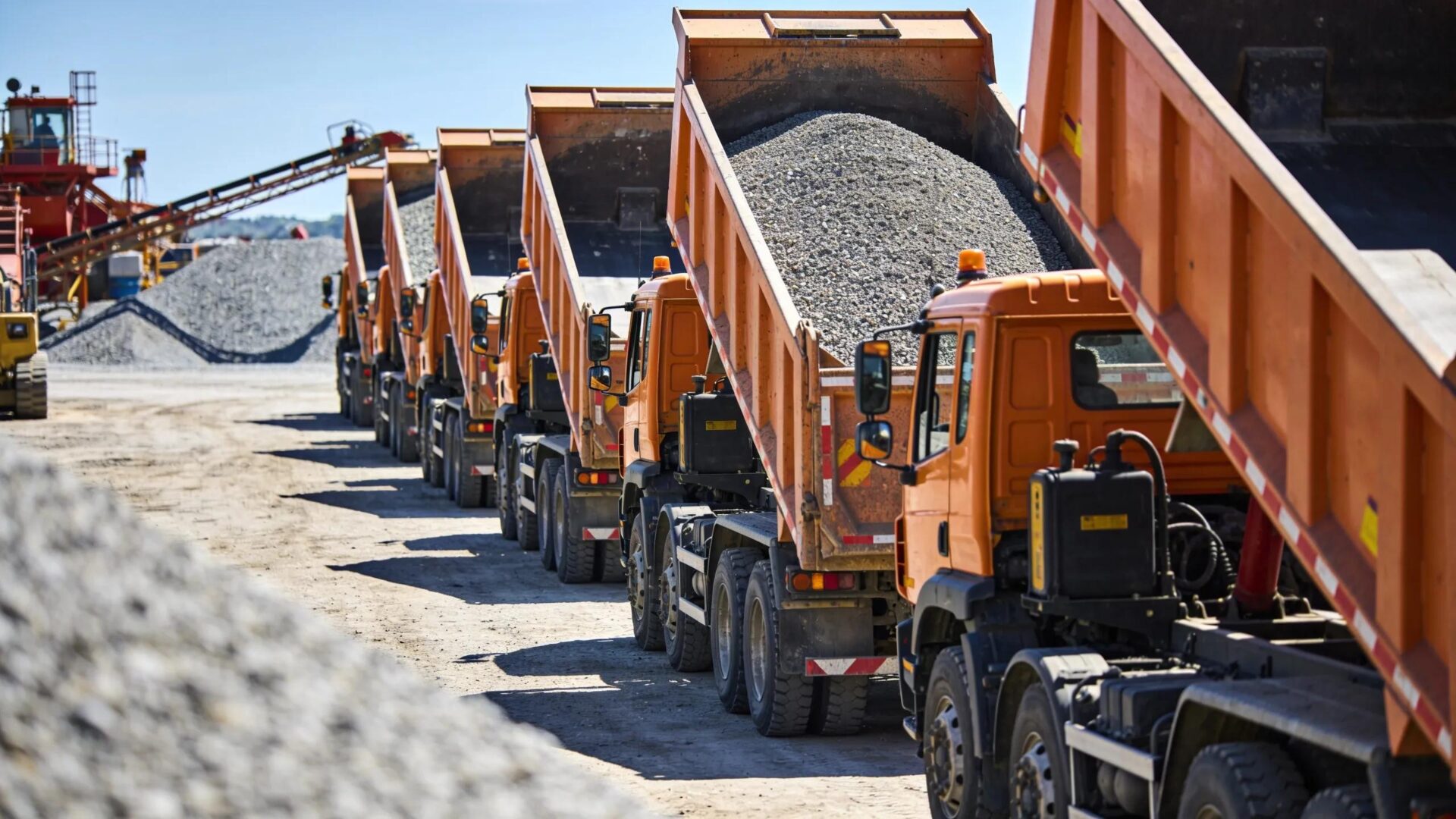 Multiple dump trucks arranged for efficient material logistics at a construction site, reinforcing aggregate delivery processes