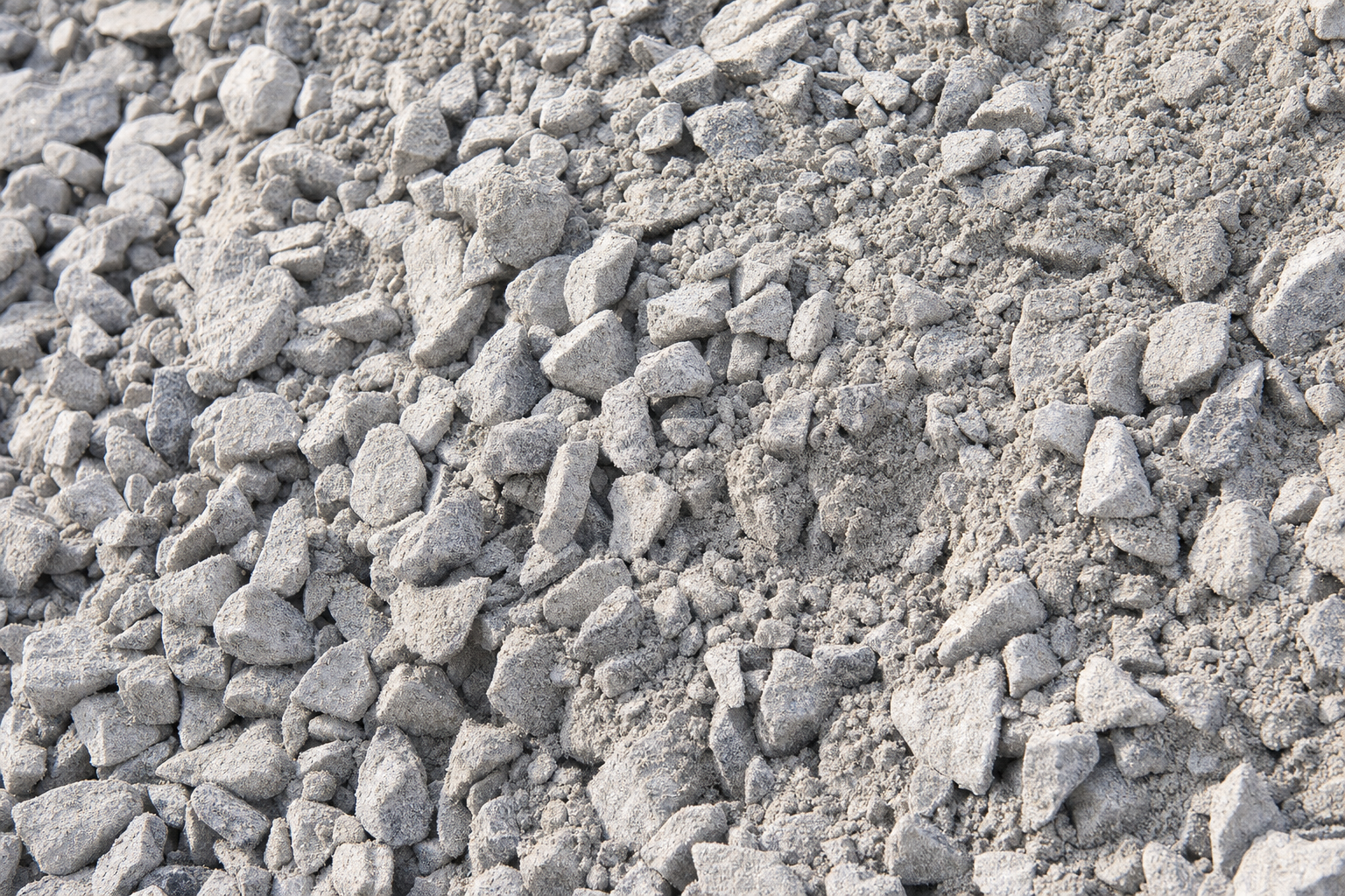 Close-up texture photograph of road base material showing mixed aggregate sizes with visible fines and dust coating on crushed limestone pieces